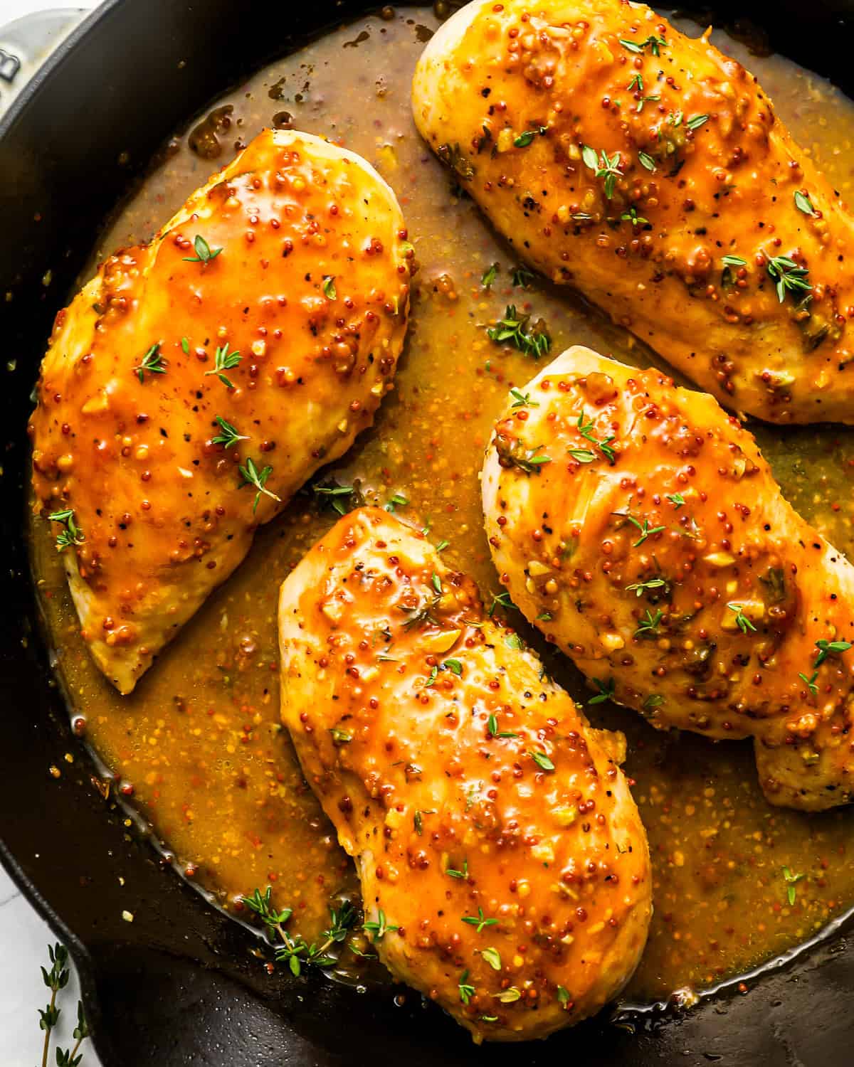 overhead view of 4 honey mustard chicken breasts in a cast iron skillet.