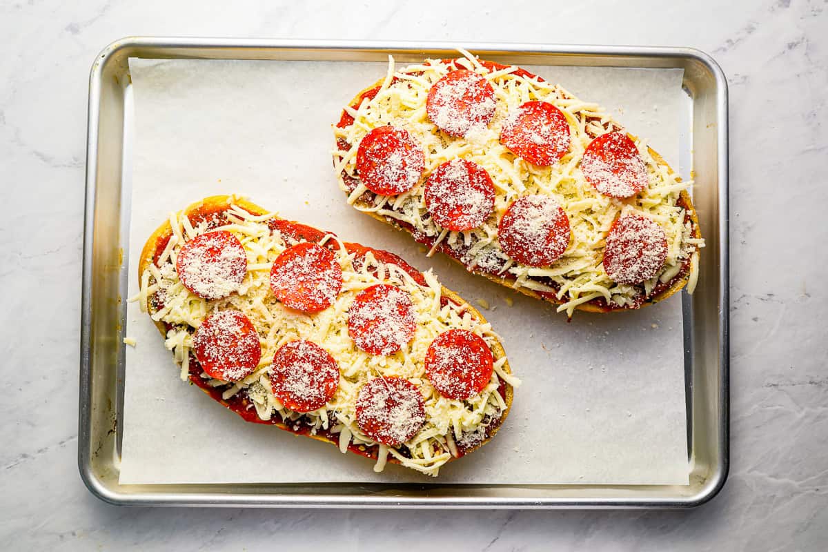 2 uncooked French bread pizzas on a baking sheet.