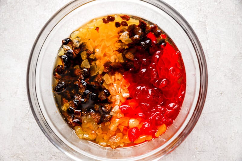 Dried and candied fruits soaking in bourbon, in a glass mixing bowl.