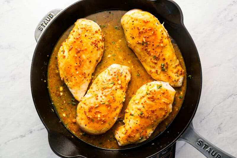 honey mustard sauce poured over seared chicken breasts in a cast iron skillet.