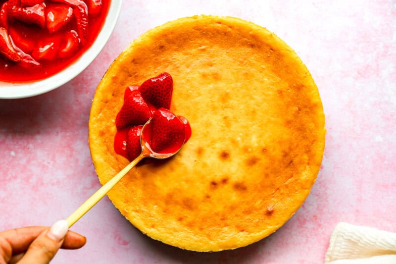 placing strawberry sauce on top of a baked cheesecake.