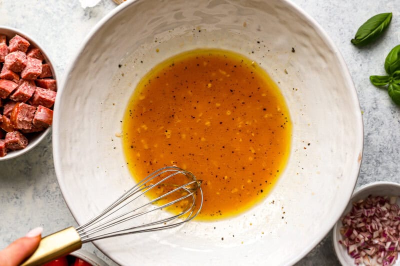 orange-brown dressing in a white bowl with a whisk.