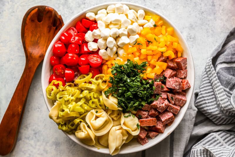 ingredients for tortellini pasta salad in a white serving bowl.