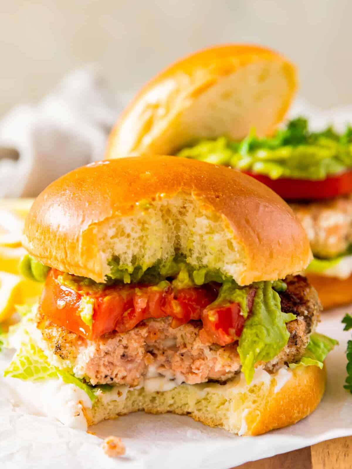 salmon burger on a bun with lettuce and tomato with a bite taken from it
