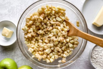 mixing diced apples with spices in a glass bowl with a wooden spoon.