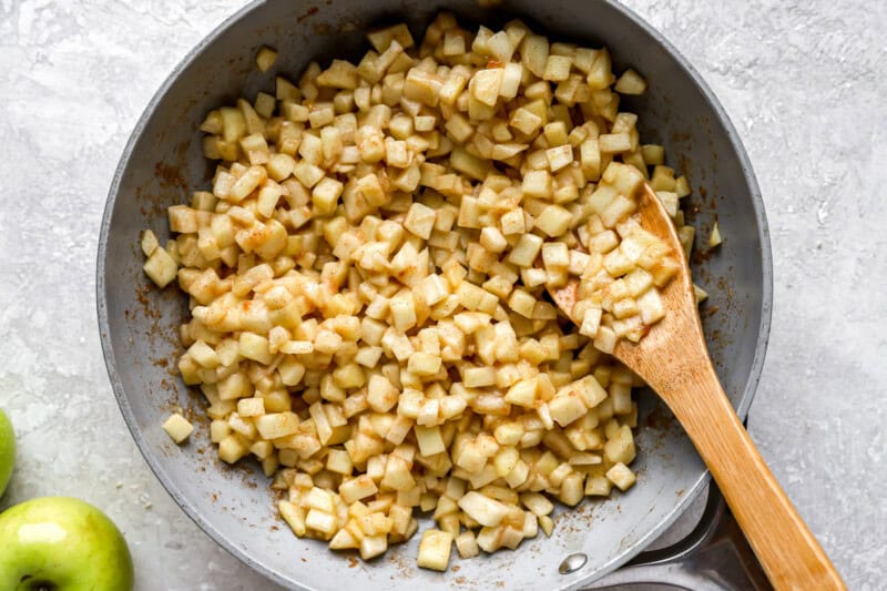 cooking diced apples in a pan with a wooden spoon.