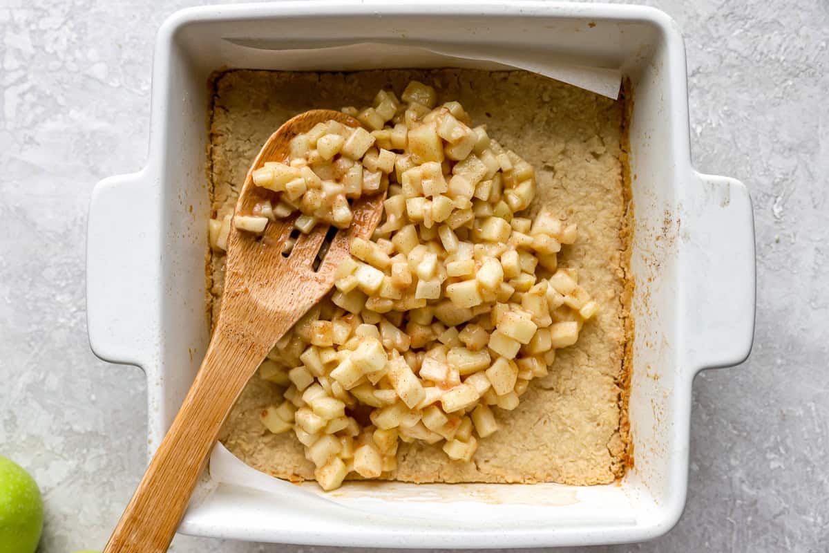 spreading apple filling over baked pie crust in a square baking dish.