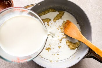 pouring milk into an onion roux in a pan with a wooden spoon.
