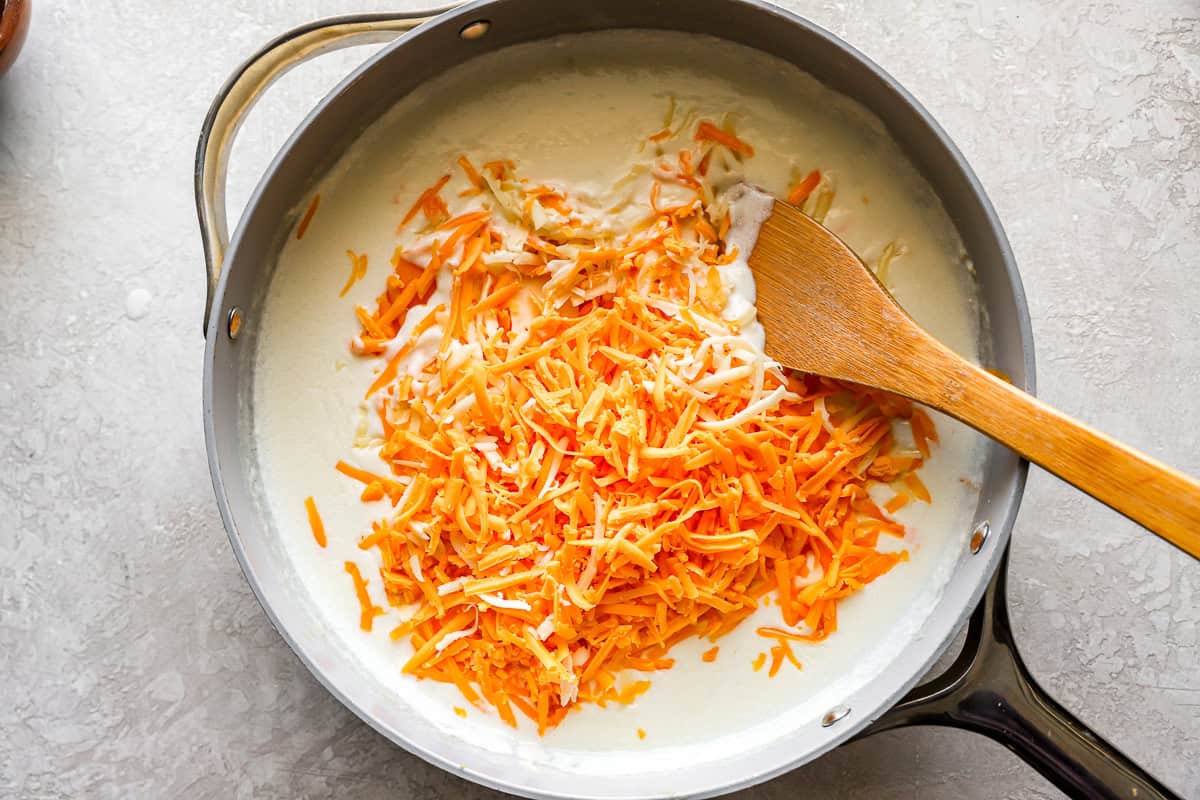 stirring shredded cheeses into white sauce in a pan with a wooden spoon.