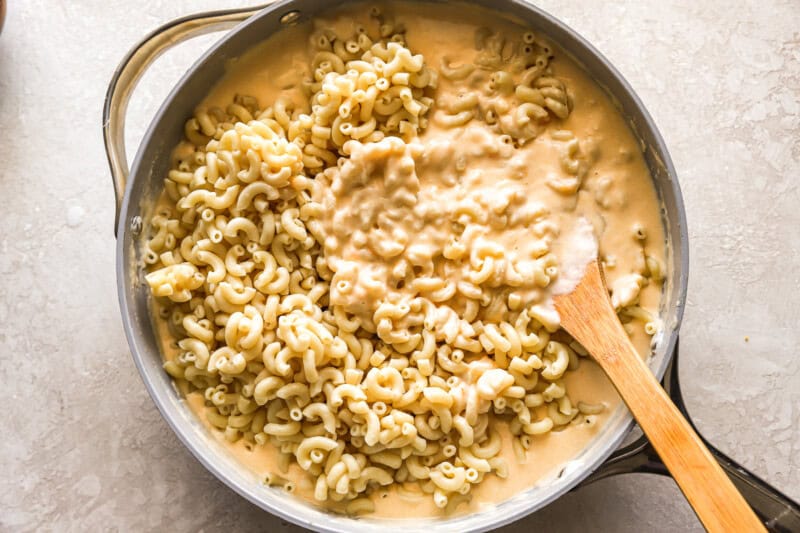 stirring cooked macaroni into cheese sauce in a pan with a wooden spoon.