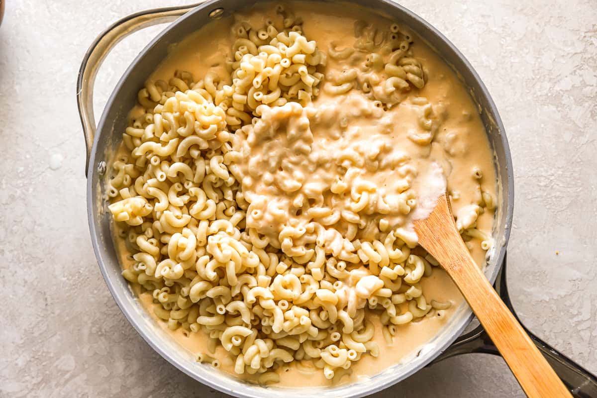stirring cooked macaroni into cheese sauce in a pan with a wooden spoon.