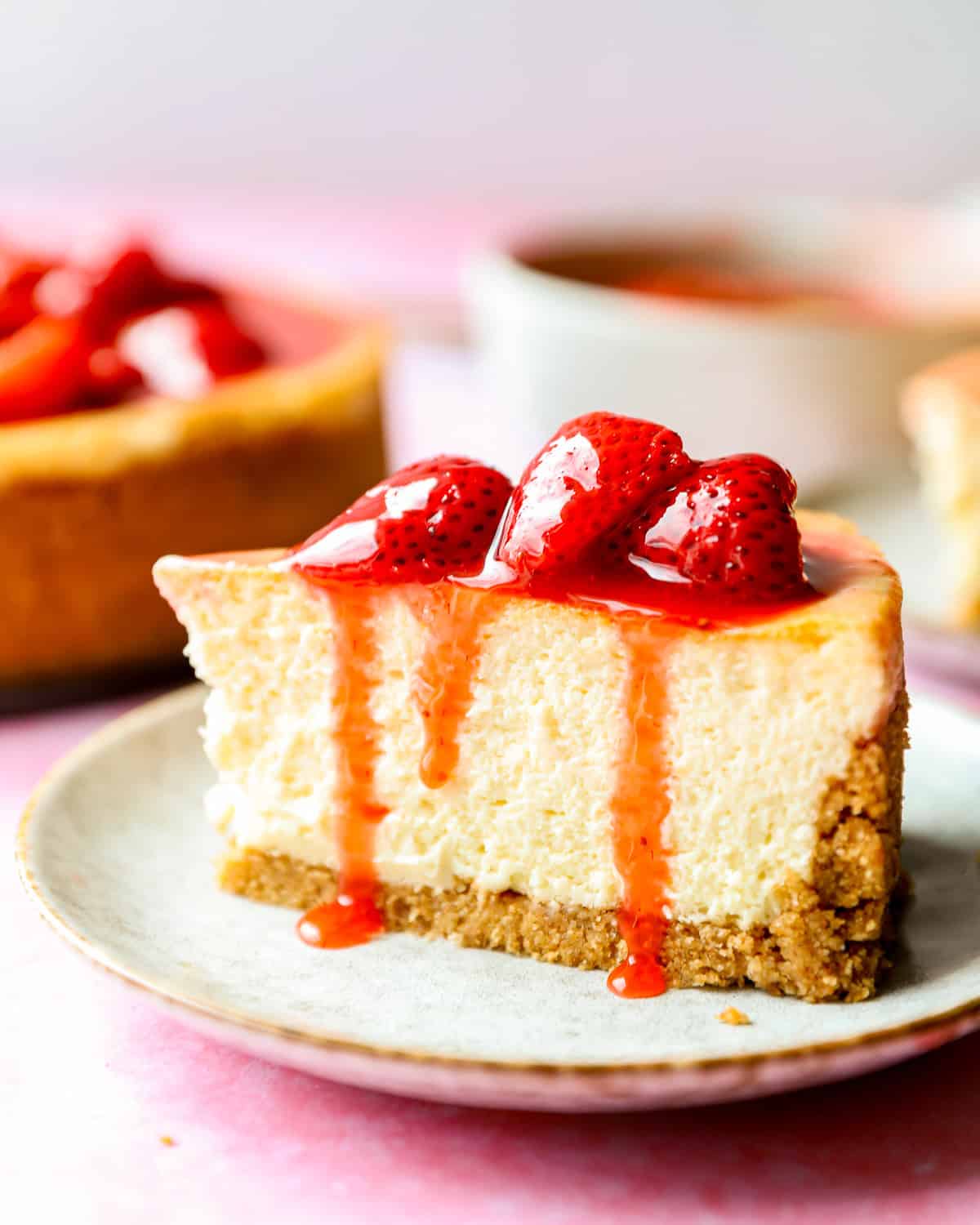 side view of a slice of cheesecake with strawberry sauce on top.