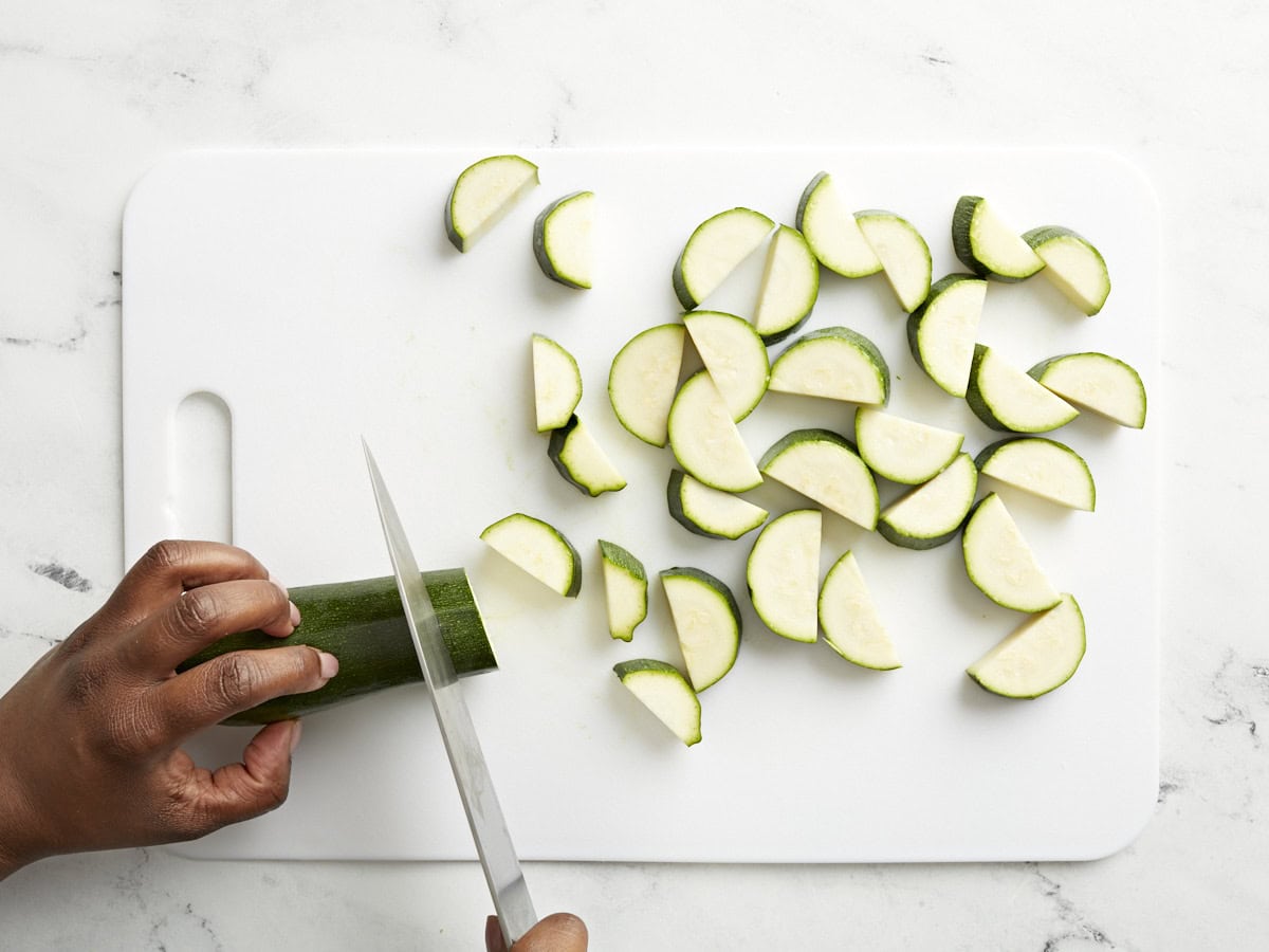 slicing zucchini into half-moons on a cutting board.