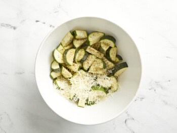 zucchini slices tossed with cheese and spices in a white bowl.