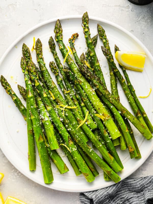 baked asparagus on a white plate with a lemon wedge.