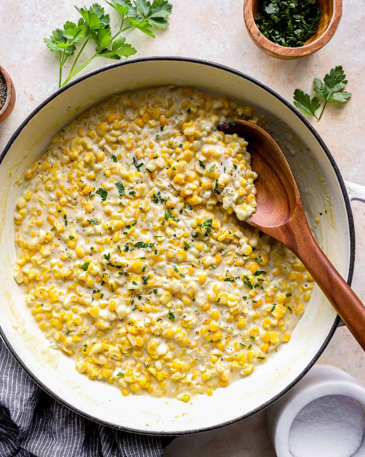 overhead view of creamed corn in a dutch oven with a wooden spoon.