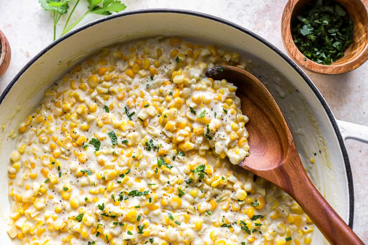 closeup view of creamed corn in a dutch oven with a wooden spoon.