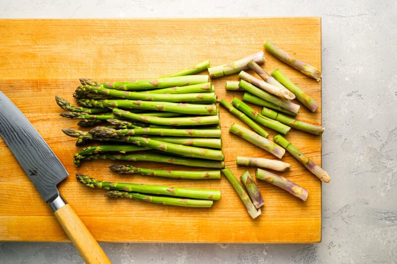 trimming the woody ends off of asparagus on a cutting board.