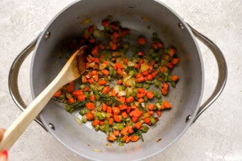 sauteeing vegetables in a large pot with a wooden spoon.