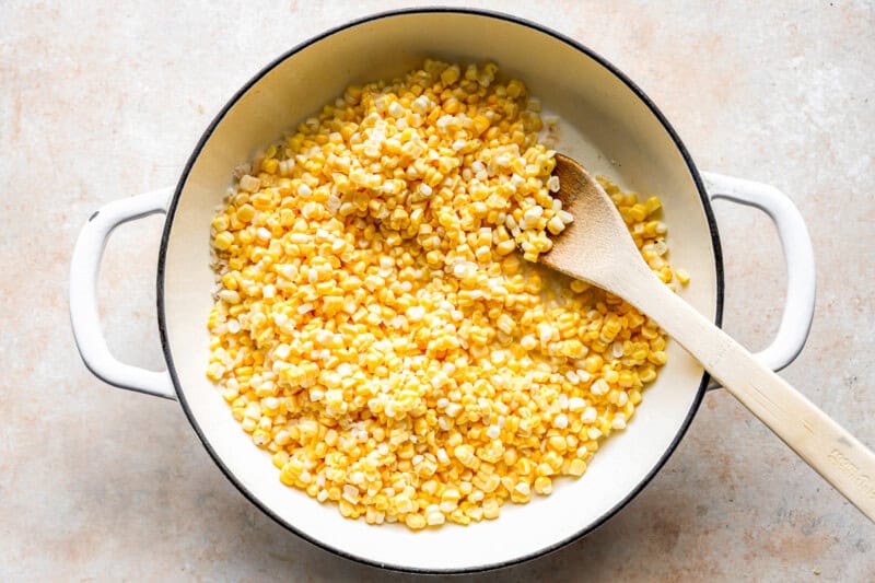 cooking corn kernels in a dutch oven with a wooden spoon.