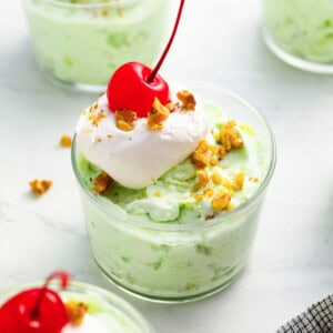 a serving of watergate salad in a glass dish with whipped cream, nuts, and a cherry on top.