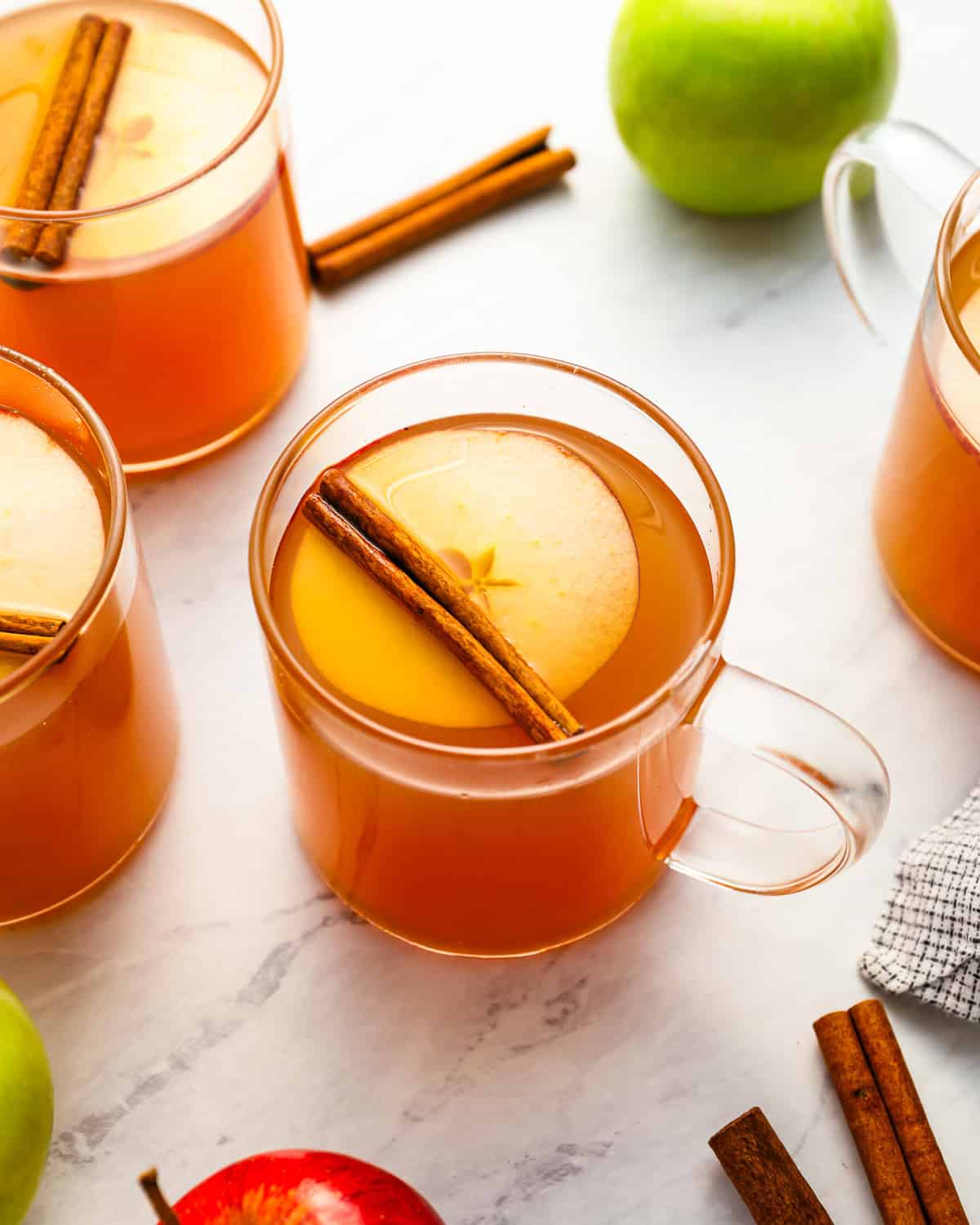 a glass of apple cider topped with an apple slice and a cinnamon stick.