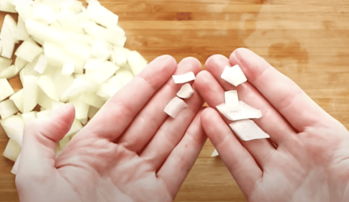 Hands holding up pieces of a diced onion to show size.