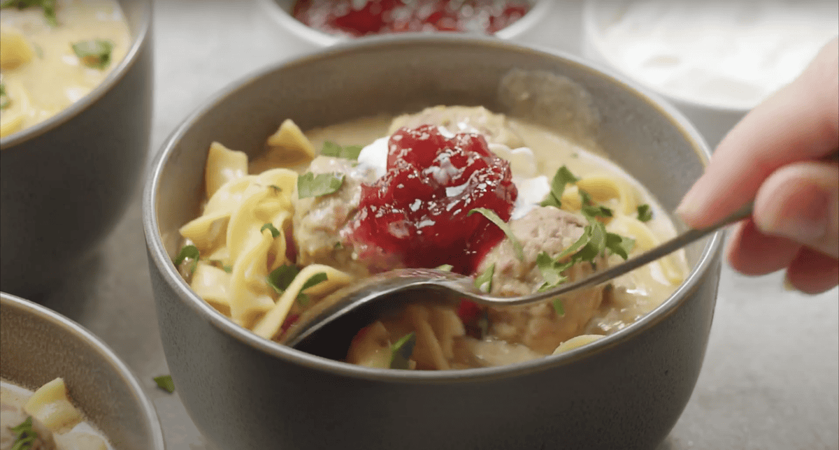 A bowl of Swedish meatball soup topped with lingonberry jam.