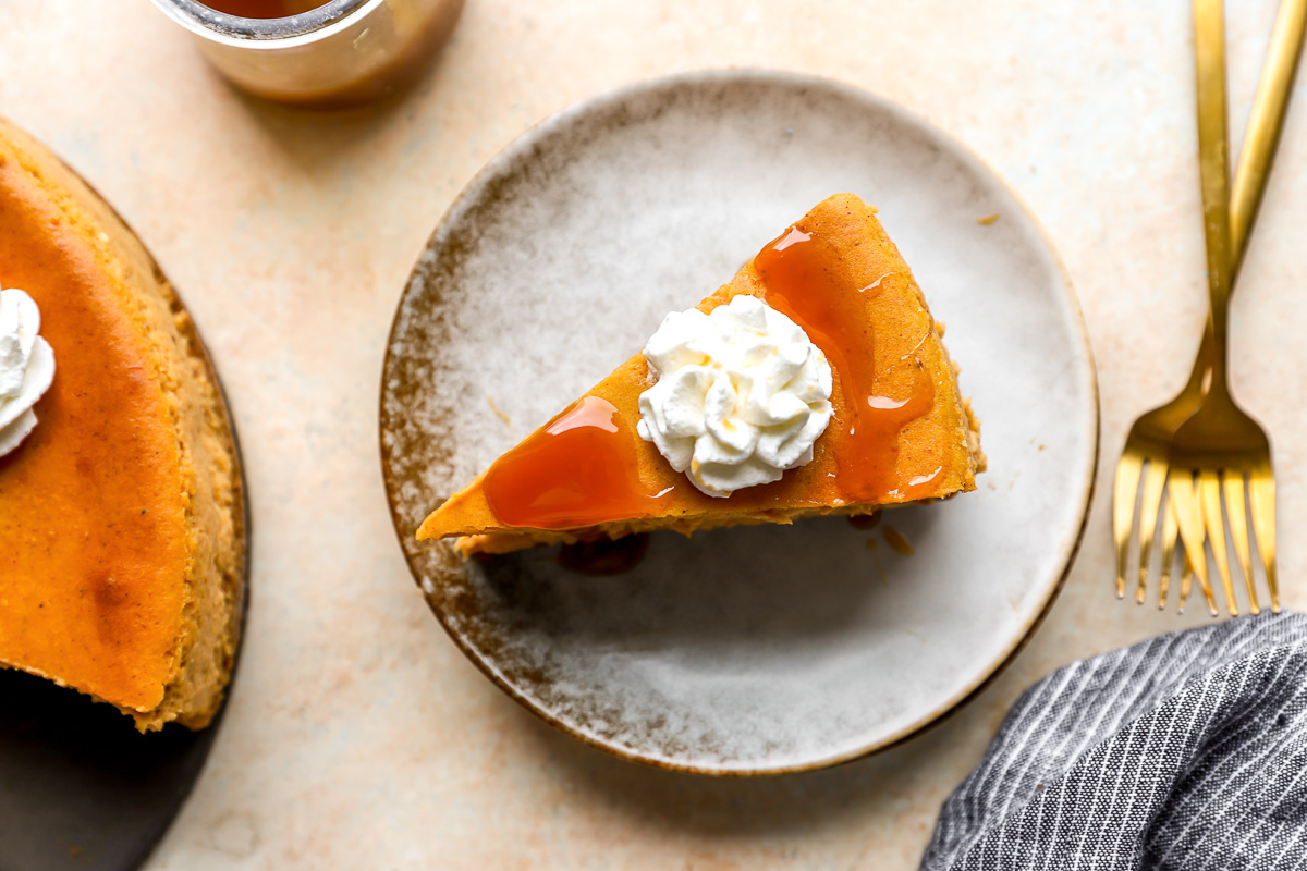 overhead view of a slice of pumpkin cheesecake on a plate with caramel sauce and whipped cream.