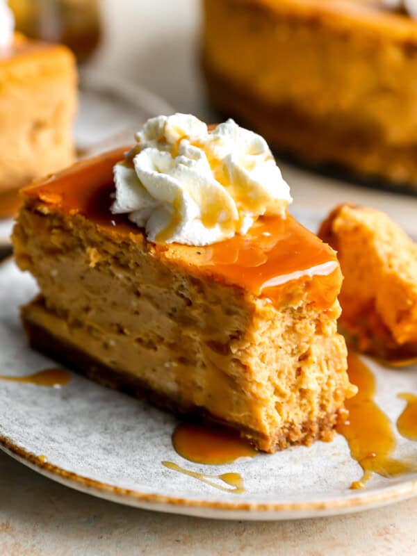 a partially eaten slice of pumpkin cheesecake on a plate with caramel sauce, whipped cream, and a fork.