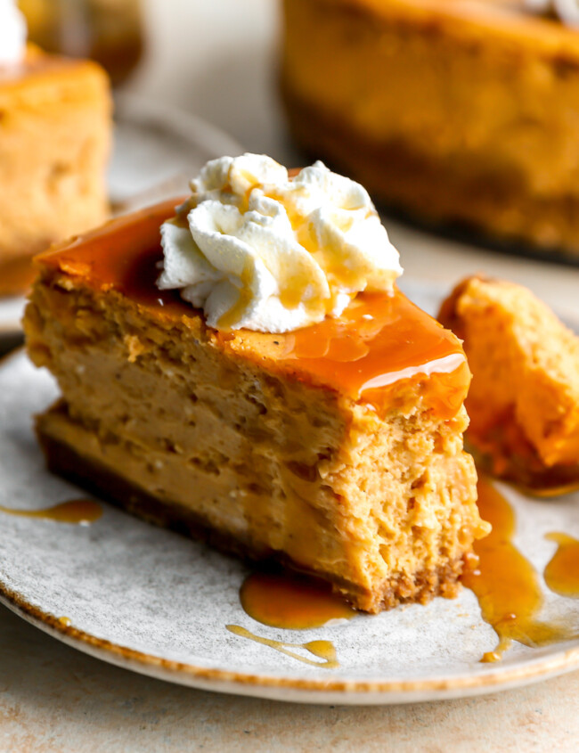 a partially eaten slice of pumpkin cheesecake on a plate with caramel sauce, whipped cream, and a fork.