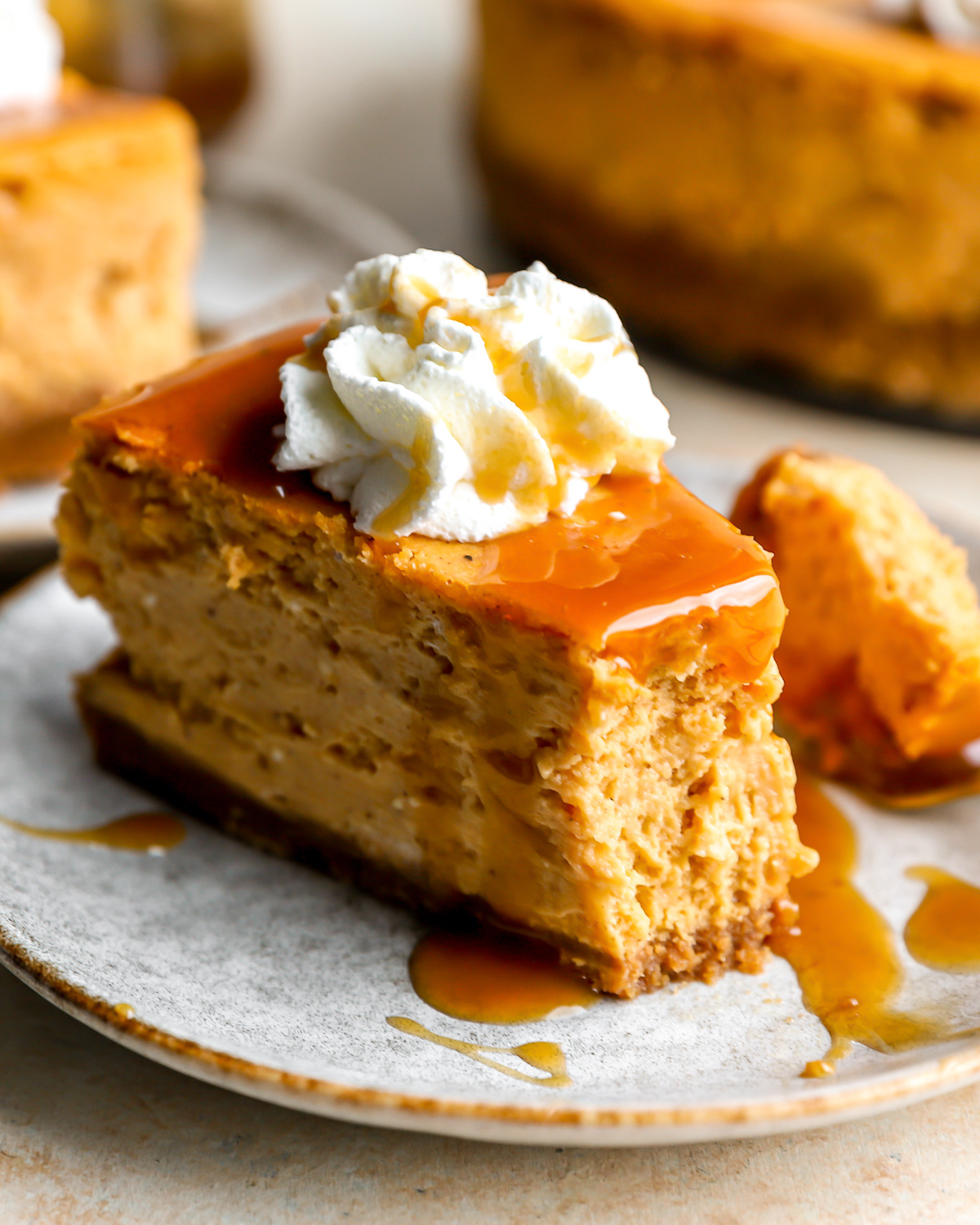 a partially eaten slice of pumpkin cheesecake on a plate with caramel sauce, whipped cream, and a fork.