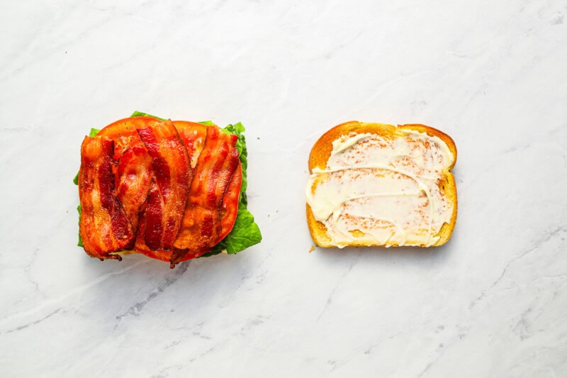 2 slices of mayo-coated toasted bread, one topped with lettuce, tomato, and bacon.