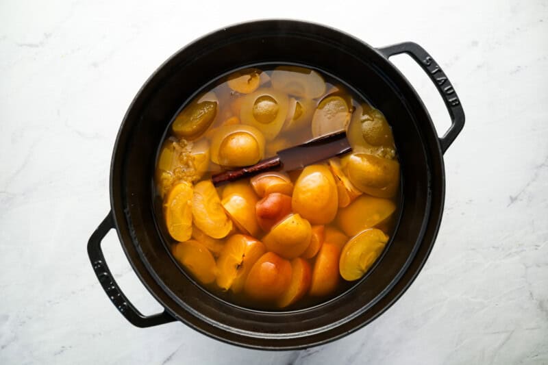 cooked apple slices, tangerines, and spices in a pot.