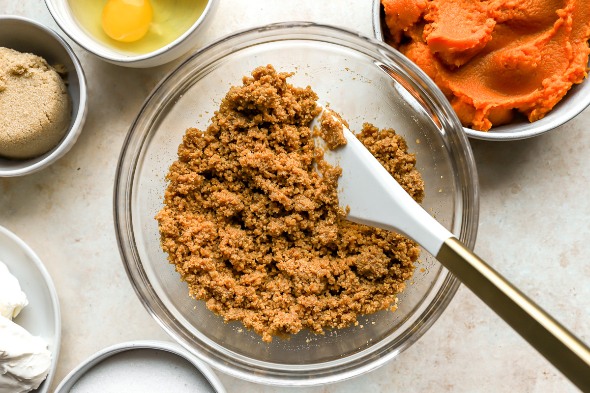 crushed graham crackers mixed with butter in a glass bowl with a rubber spatula.