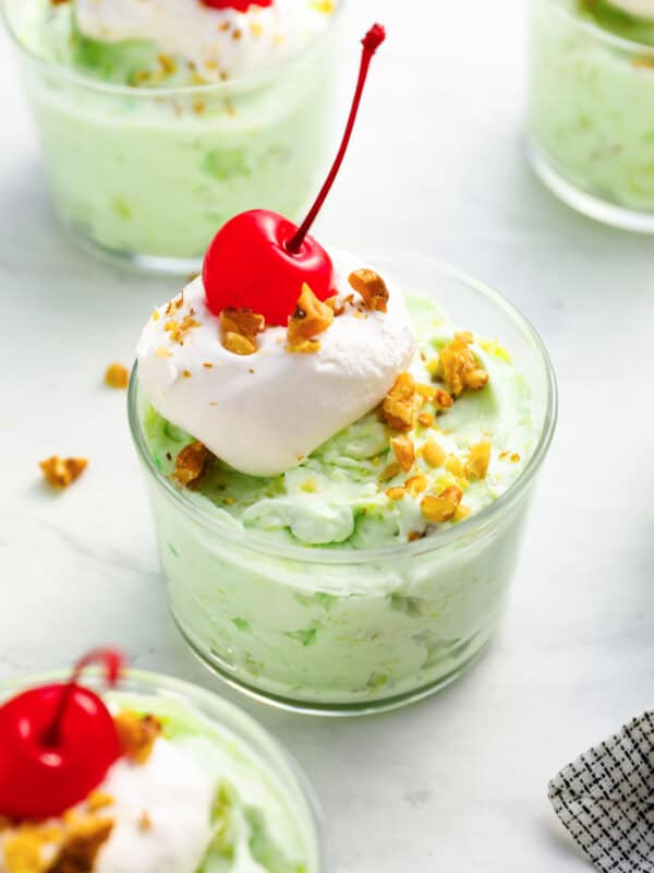 a serving of watergate salad in a glass dish with whipped cream, nuts, and a cherry on top.