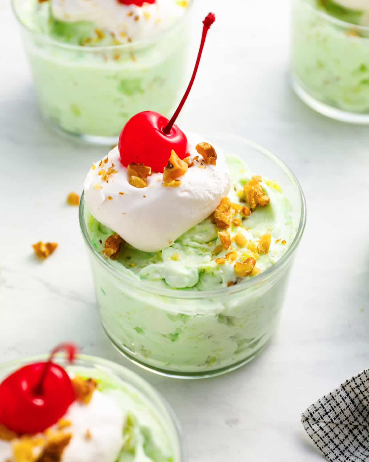 a serving of watergate salad in a glass dish with whipped cream, nuts, and a cherry on top.