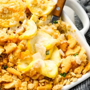 a wooden spoon lifting a scoop of squash casserole from a baking dish.