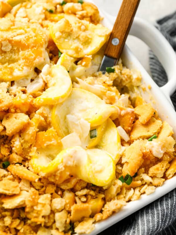 a wooden spoon lifting a scoop of squash casserole from a baking dish.