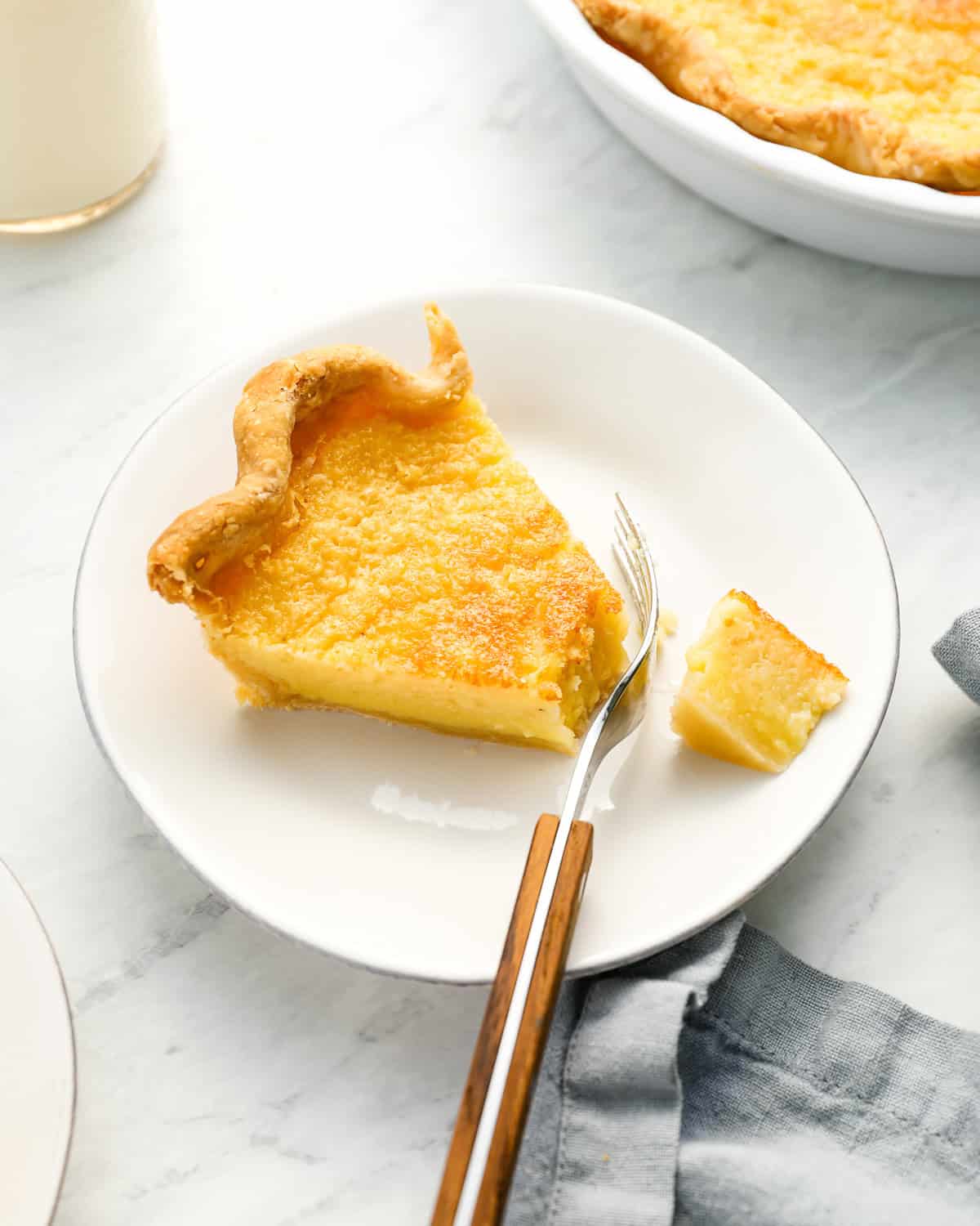 a cut slice of buttermilk pie on a white plate with a fork.