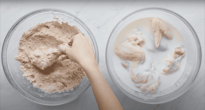 Dredging a piece of chicken in seasoned flour.