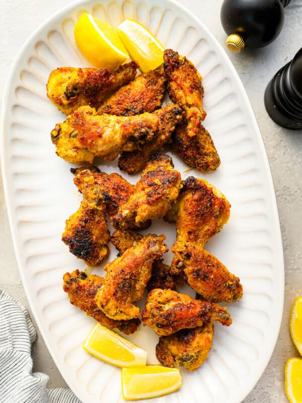 a bunch of crispy lemon pepper wings on a white serving platter with lemon slices