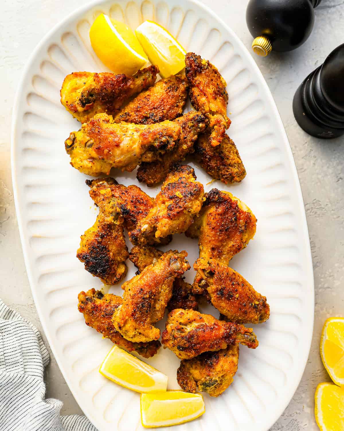 a bunch of crispy lemon pepper wings on a white serving platter with lemon slices