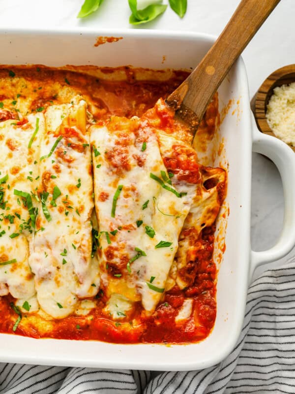 baked manicotti being served with wooden spoon from a white baking dish