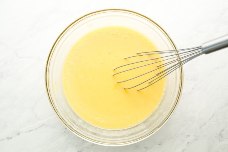 buttermilk pie filling in a glass bowl with a whisk.