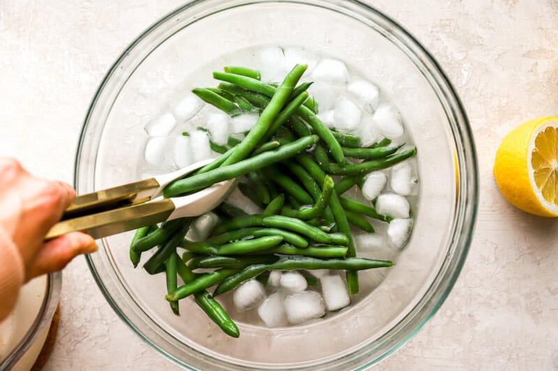 placing cooked green beans in ice water in a glass bowl.