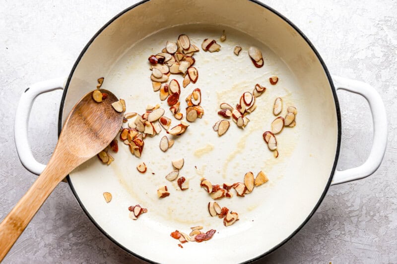 toasting sliced almonds in a pan with a wooden spoon.