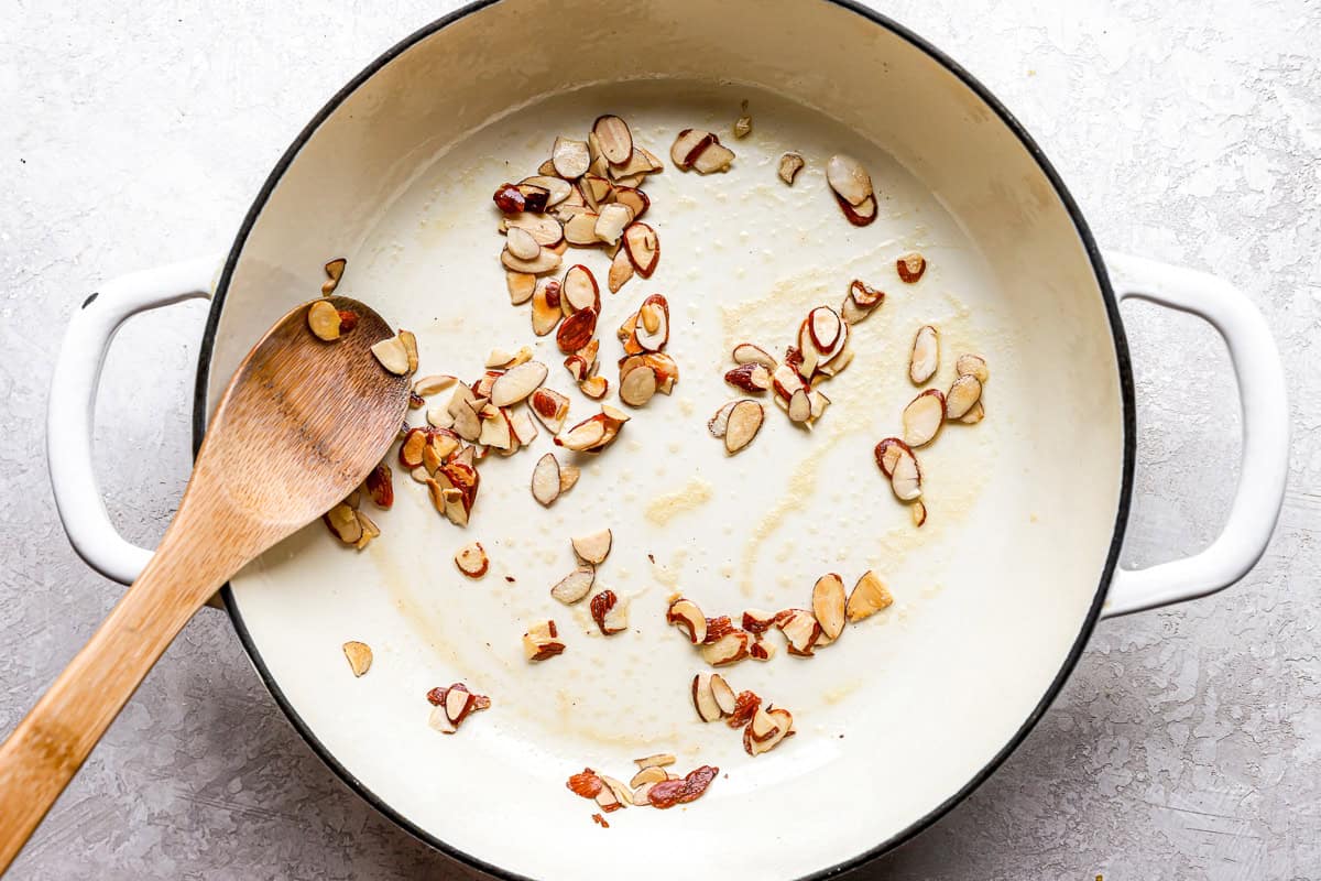 toasting sliced almonds in a pan with a wooden spoon.