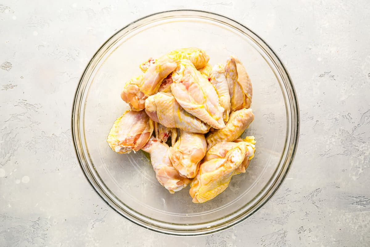 raw chicken wings tossed with melted butter in a glass bowl