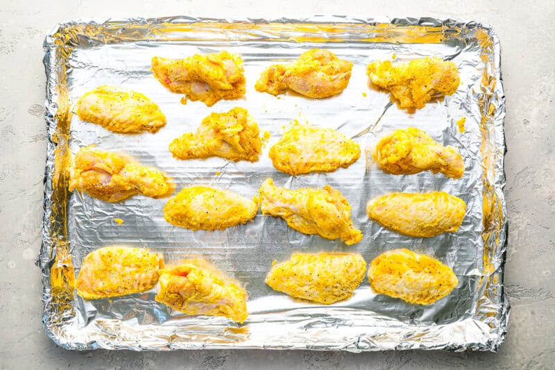 raw chicken wings tossed in flour and lemon pepper butter lined on a baking sheet covered in foil